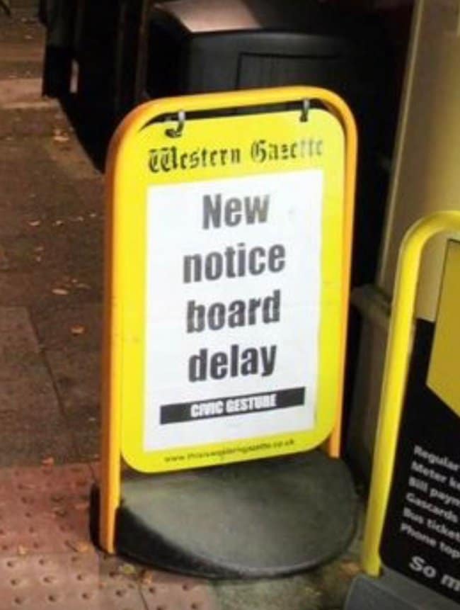 A beautifully recursive logistical failure archived as a funny news headline captures a yellow roadside sandwich board for the Western Gazette that features a printed flyer announcing: "New notice board delay."