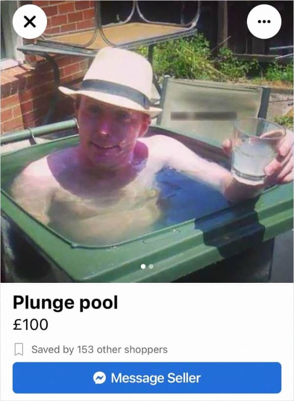 A man in a fedora hat relaxing inside an outdoor green garbage bin filled with water.