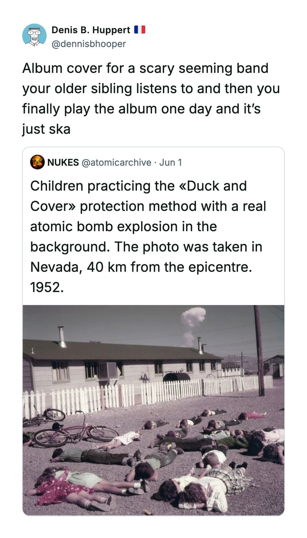 Historical photograph inside a funny quote tweet by Denis B. Huppert showing a 1952 Nevada nuclear test "Duck and Cover" drill with children lying on the ground.