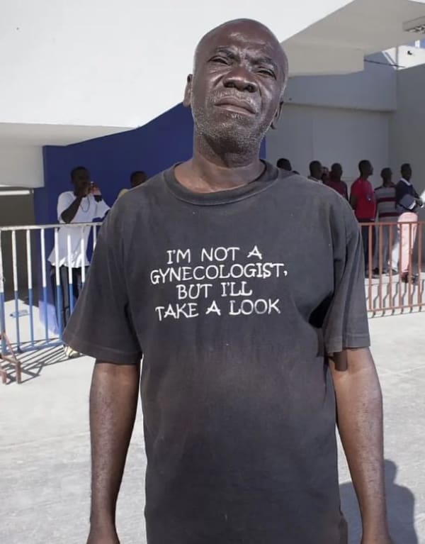 highly inappropriate funny t shirt worn by an older man looking directly into the camera, featuring white text on black cotton that reads: "I'M NOT A GYNECOLOGIST, BUT I'LL TAKE A LOOK."