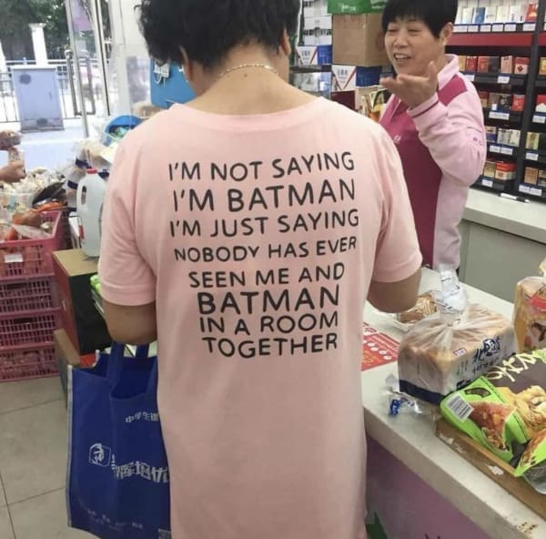 A superhero-themed funny t shirt spotted on a woman shopping at a convenience store checkout, displaying the classic logic puzzle in black text on a pink dress-shirt: "I'M NOT SAYING I'M BATMAN I'M JUST SAYING NOBODY HAS EVER SEEN ME AND BATMAN IN A ROOM TOGETHER."