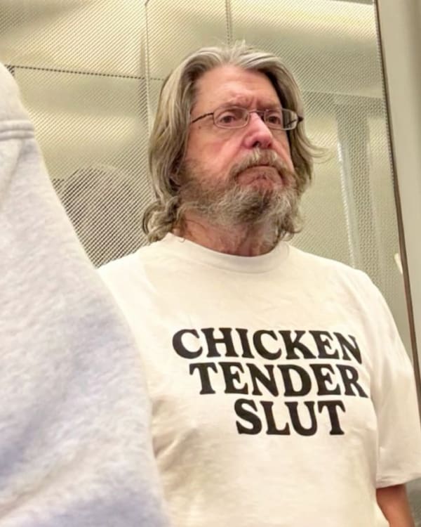 A delightfully straightforward funny t shirt worn by an older gentleman with glasses and a grey beard, loudly proclaiming his dietary preferences with the text: "CHICKEN TENDER SLUT."