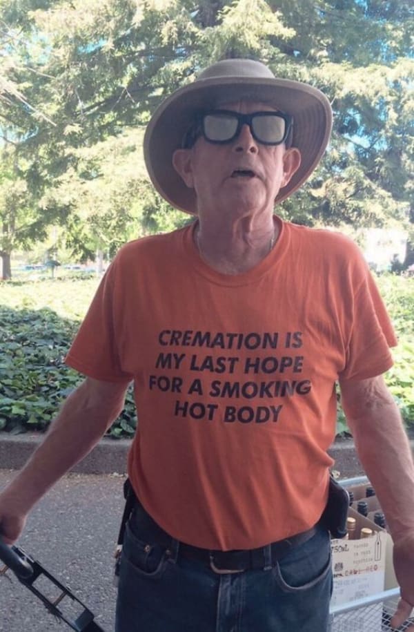A morbidly hilarious funny t shirt worn by a senior citizen in dark sunglasses and a sun hat, displaying bold black letters on a bright orange background stating: "CREMATION IS MY LAST HOPE FOR A SMOKING HOT BODY."