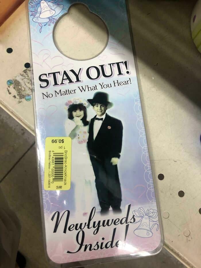 An incredibly bizarre funny thrift store find showing a pastel door-hanger sign featuring a photo of a young boy in a tuxedo and a little girl in a bride costume, accompanied by deeply threatening text reading: "STAY OUT! No Matter What You Hear! Newlyweds Inside!"