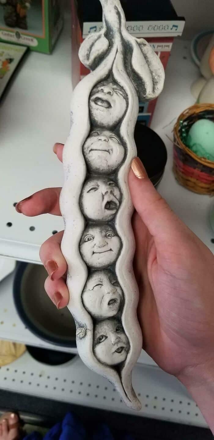 A highly cursed ceramic decoration categorized as a funny thrift store find, showing a long, curved white pea pod where the individual round "peas" inside are sculpted as five realistic, deeply distressed, groaning human faces.