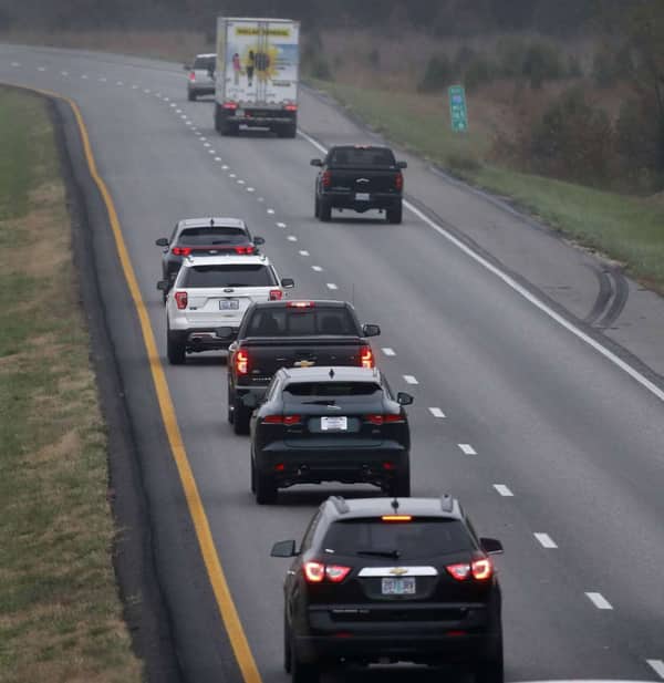 A line of cars driving in reverse formation on the shoulder of a highway lane.