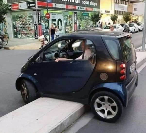 A small blue smart car completely high-centered and stuck on top of a concrete median curb.