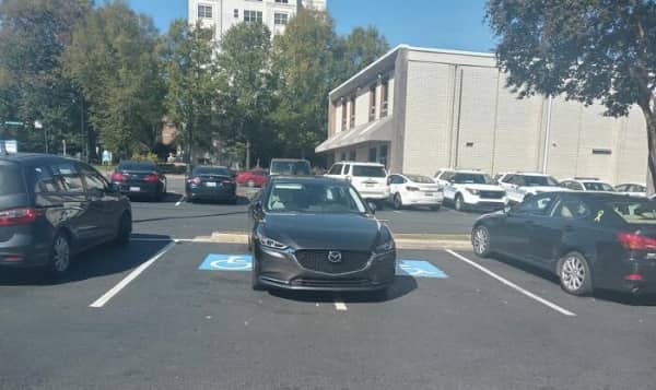 A dark grey sedan parked horizontally across two adjacent blue painted handicap parking spots.