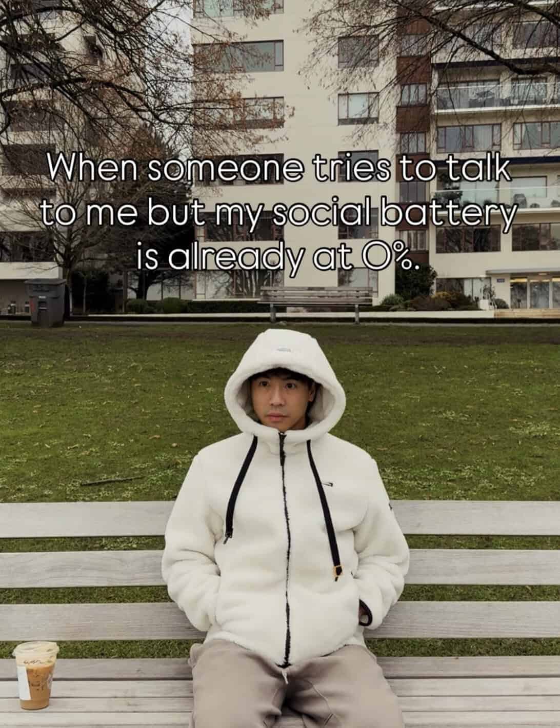 Person in a white hooded jacket staring blankly into space on a park bench.