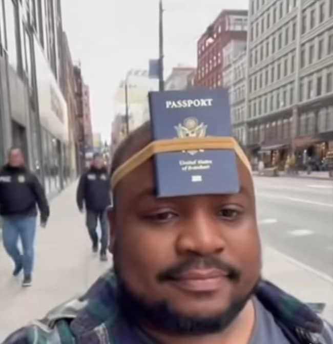 A man walking down a city street with an American passport strapped to his forehead.