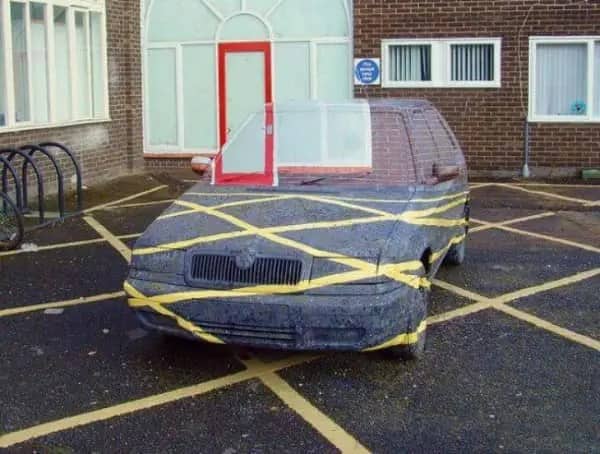 A parked car completely wrapped in yellow hazard tape to match the parking lines below.