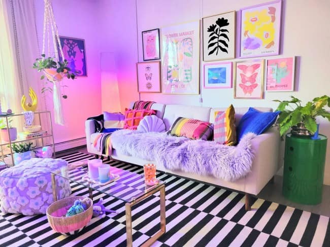 A retro-modern apartment living room using dopamine-fueled maximalist interior design elements, showcasing a striking black-and-white checkered floor carpet, a neutral sofa topped with a shaggy lavender faux-fur throw, and a colorful abstract gallery wall under neon ambient lighting.