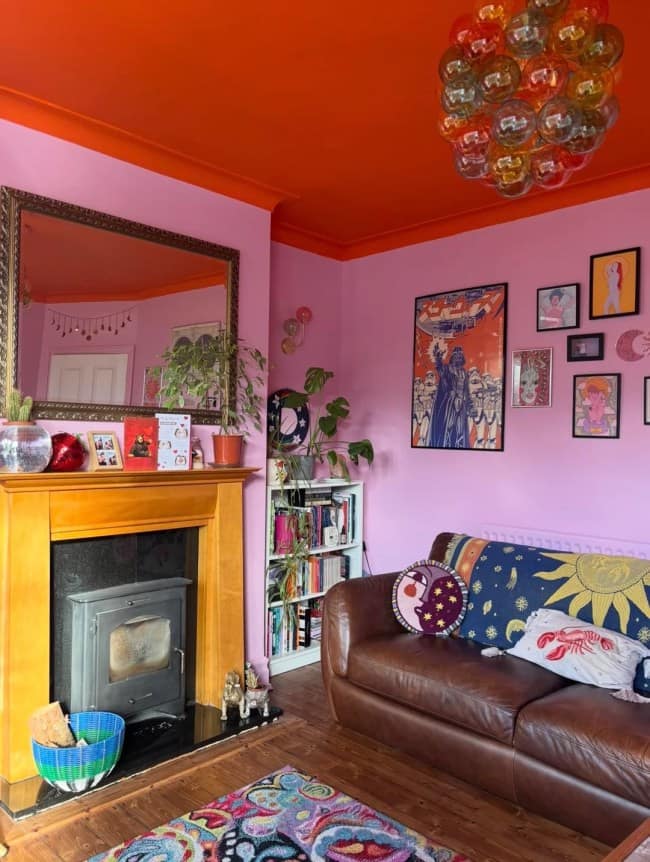moody, eclectic sitting room celebrating vibrant maximalist interior design with soft lavender walls, a jaw-dropping bright orange ceiling, a brown leather couch piled with celestial throw pillows, and a custom gallery wall featuring a pop-art Darth Vader print.