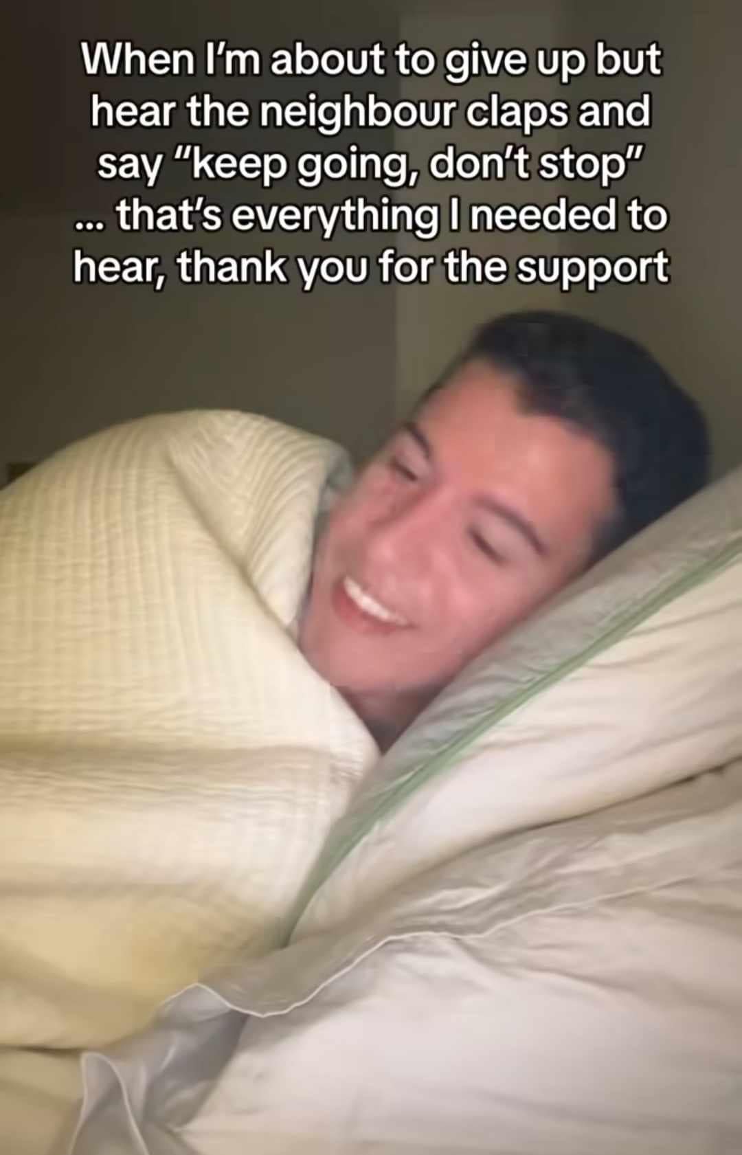 A humorous funny meme layout showing a close-up photo of a young man smiling widely under bed covers, paired with text misinterpreting thin-walled apartment noises as motivational workout support.