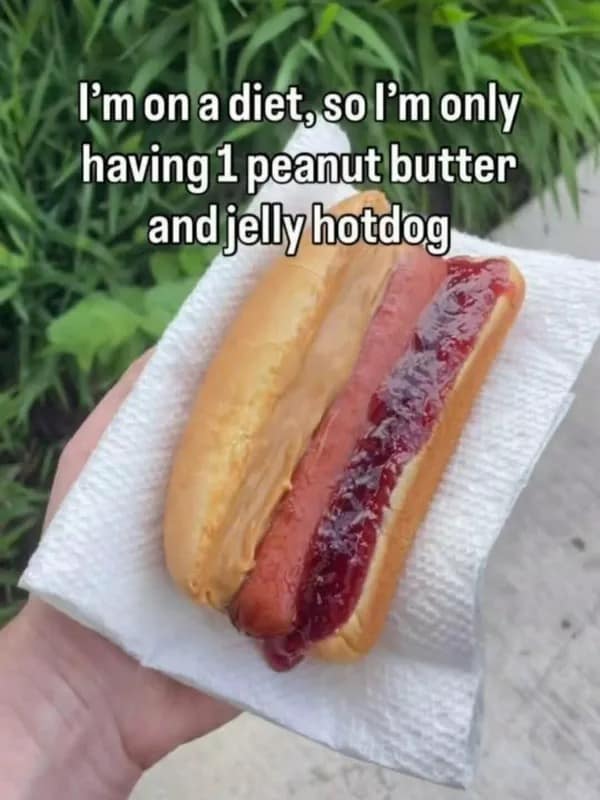 A meme dump culinary crime image displaying a hand holding a standard hot dog bun loaded with a cooked sausage link, heavily slathered with creamy peanut butter on one side and sweet fruit jelly on the other, captioned: "I'm on a diet, so I'm only having 1 peanut butter and jelly hotdog".
