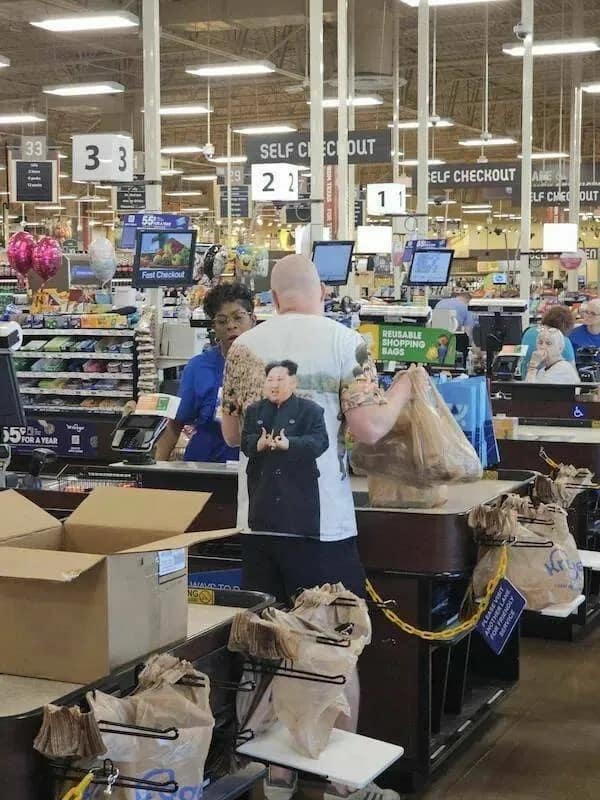 Kim Jong Un graphic t-shirt worn by a shopper at a grocery store checkout register in a meme dump photo.