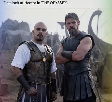 A hilarious cinematic crossover image in a meme dump titled "First look at Hector in 'THE ODYSSEY'," placing a modern cholo character wearing an oversized white t-shirt and polished bronze plate armor shoulder-to-shoulder with a rugged ancient Greek warrior.