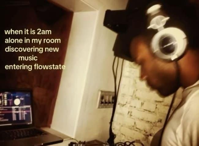 A late-night focus music meme depicting a producer in a dark bedroom wearing studio headphones and entering a deep creative flow state at 2:00 AM while discovering new tracks on his laptop.