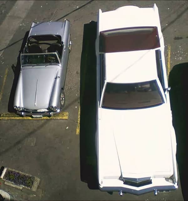 Overhead view of a compact classic convertible parked directly next to a massive vintage white luxury car.