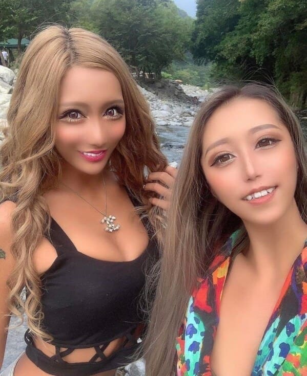 An outdoor selfie of two women whose faces have been heavily processed through extreme digital filters, expanding their eyes and narrowing their jaws into an alien-like photoshop fail.