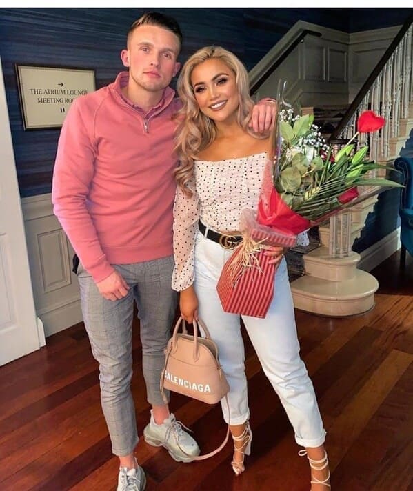A couple posing together indoors where a bizarre layering or cropping error shows the man's right leg seamlessly terminating in a woman's strappy high-heel shoe, a mind-bending photoshop fail.