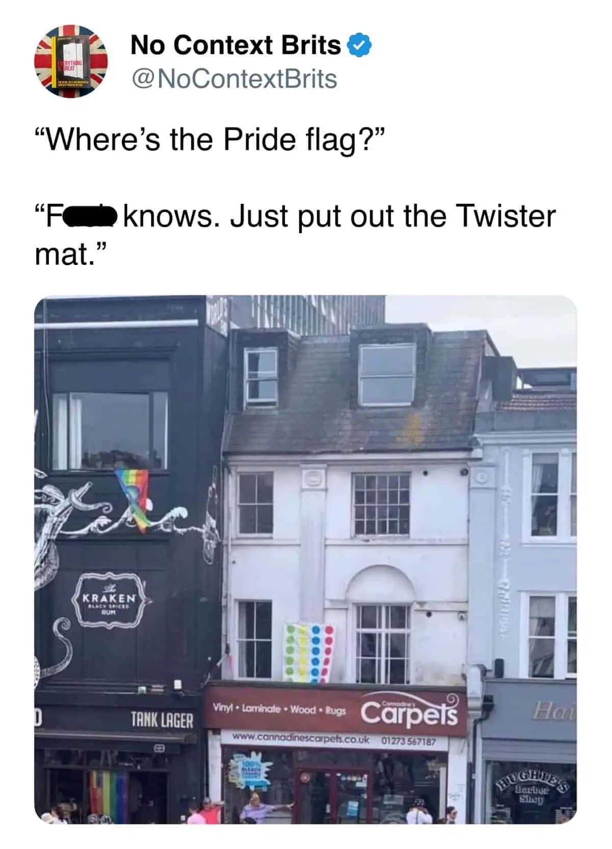 A hilarious UK architectural oversight captured as a pride meme by No Context Brits, showing a white building where someone hung a colorful dotted Twister mat out the window as a makeshift flag next to an adjacent pub flying an actual rainbow flag.