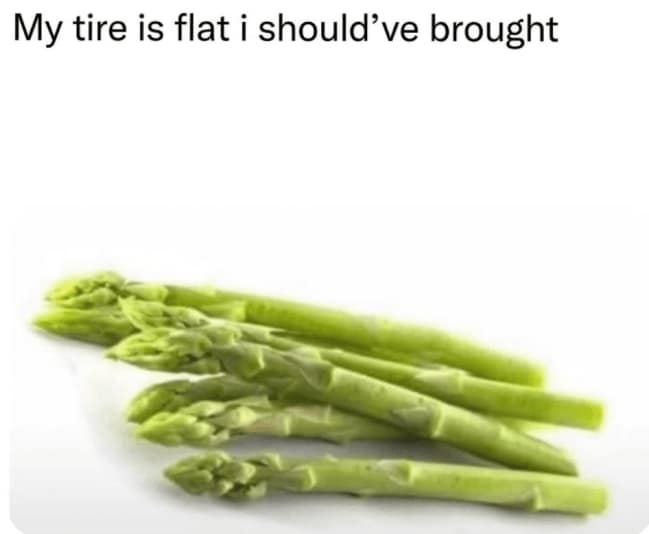 This bright studio funny pun graphic showcases a fresh bunch of green asparagus spears resting on a stark white background. The image is topped with a casual caption text layer reading, "My tire is flat i should've brought," leaning heavily into the phonetic audio joke of "a spare, I guess."