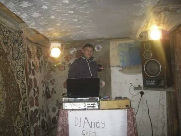 DJ Andy Chem standing at his laptop setup inside a room with carpet covered walls.