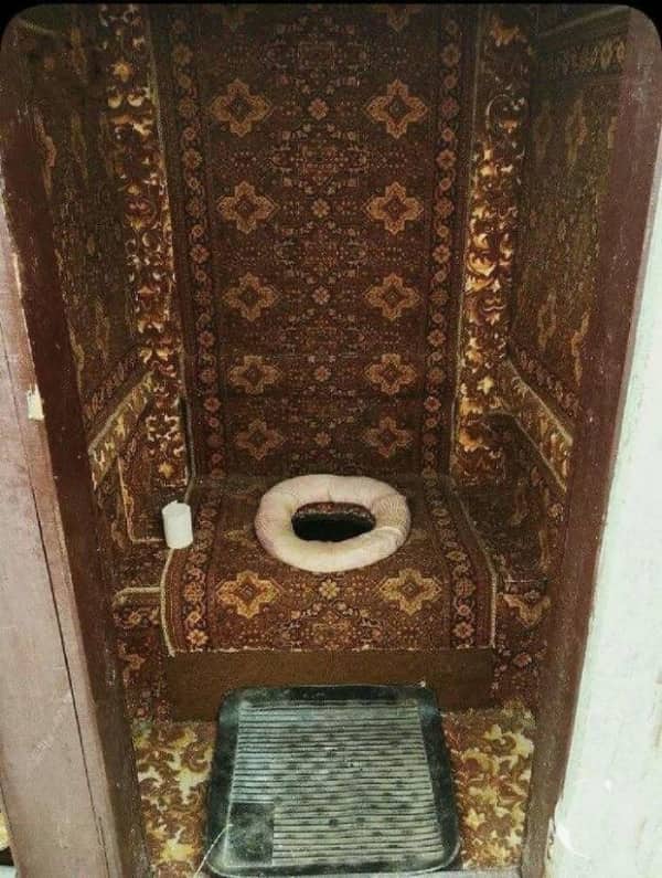 A tiny outhouse bathroom entirely lined from floor to ceiling with ornate brown patterned carpets.