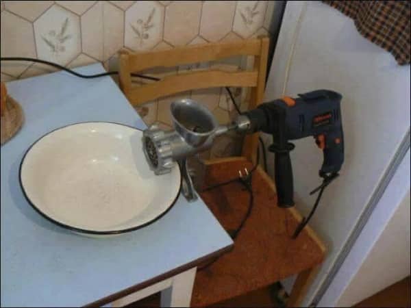 A handheld power drill rigged up directly to power a metal vintage meat grinder machine. Cap