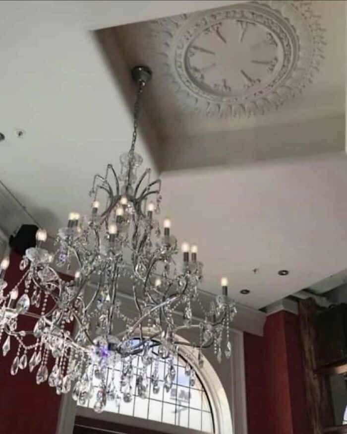 An elaborate crystal chandelier hanging completely off-center, several feet away from its decorative plaster ceiling medallion, in a glaring interior lighting design fail.