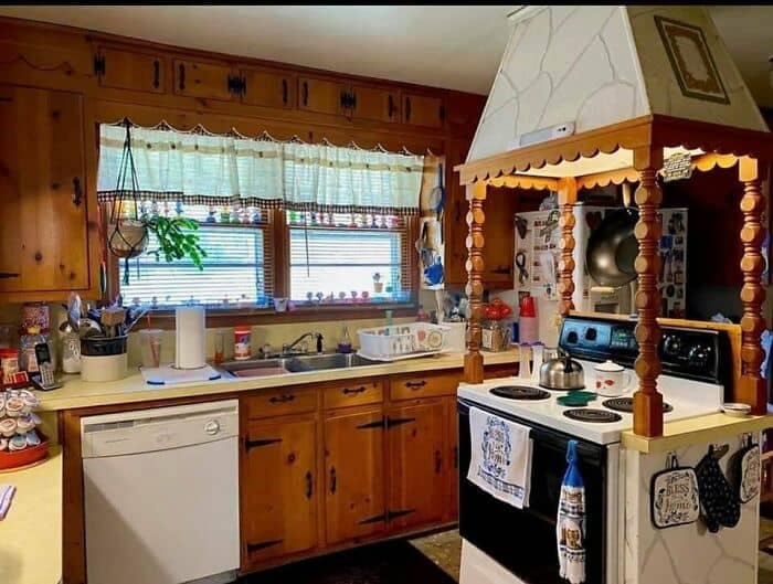 A rustic kitchen featuring heavy knotty-pine cabinets and an oversized, theatrical wooden range hood canopy supported by chunky spindle pillars in a maximalist design fail.