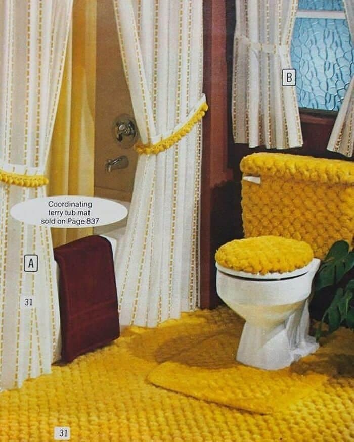 A vintage catalog print showing a bathroom completely blanketed in thick, bright yellow shag carpeting that extends onto the toilet seat cover, tank, and floor mats in a retro design fail.