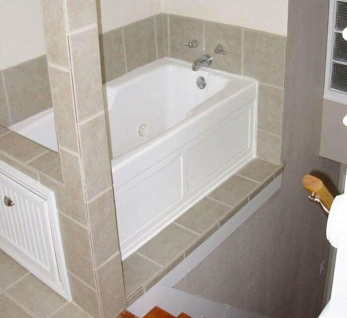 A white bathtub installed directly on a narrow tiled ledge over an open staircase drop-off, illustrating a hazardous structural design fail.