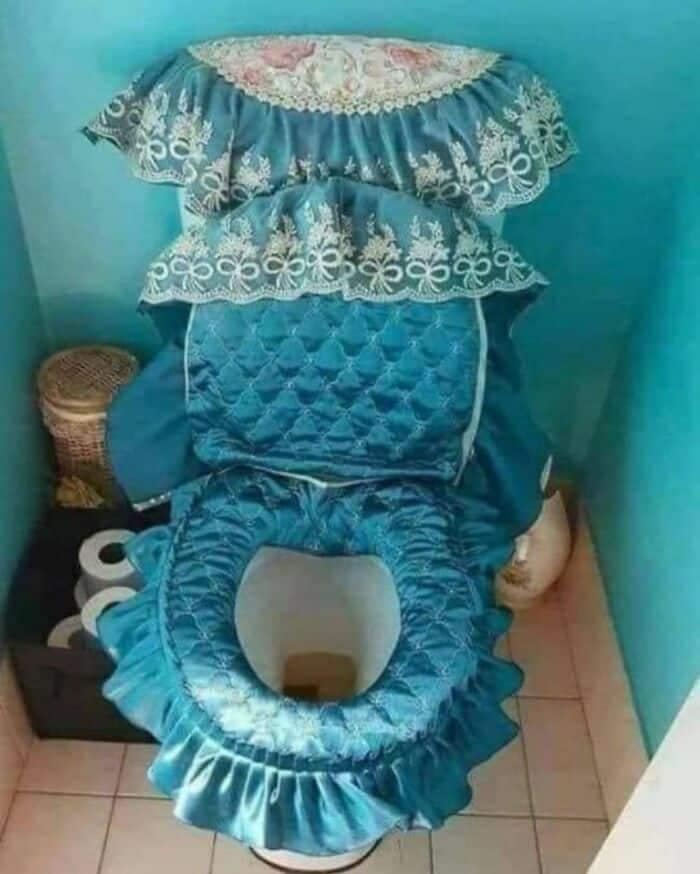 A toilet completely wrapped in heavily ruffled, quilted teal satin fabric covers from the seat to the tank, capturing a plush version of weird home decor.
