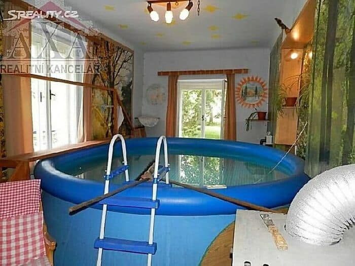 A massive blue inflatable above-ground swimming pool with a plastic ladder shoved completely inside a standard residential room, demonstrating a chaotic design fail.