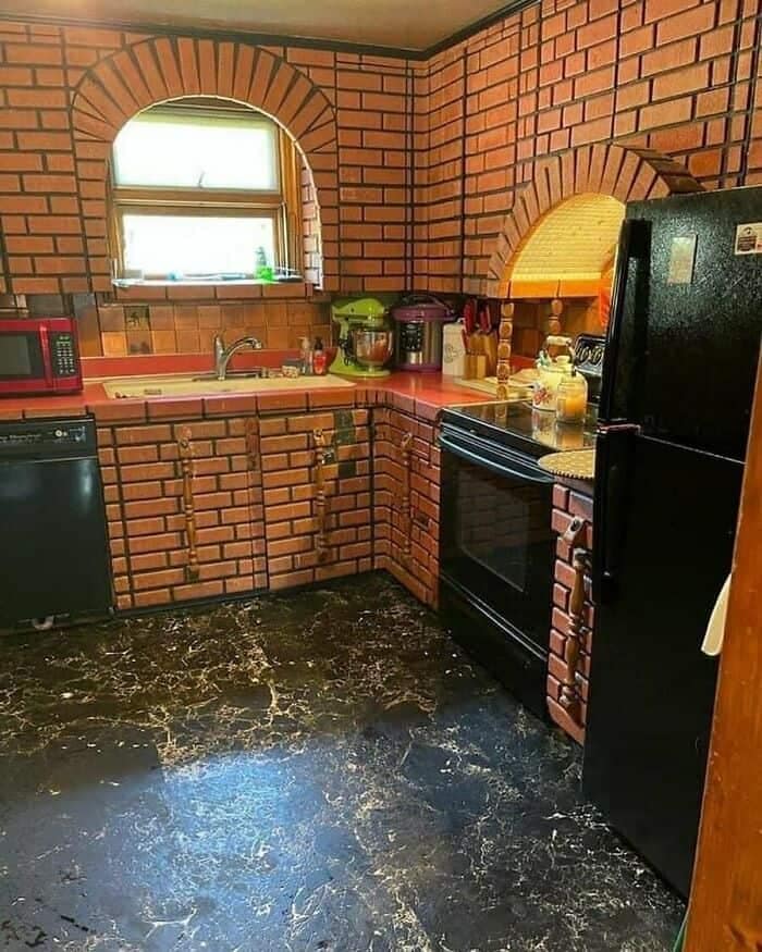 A kitchen interior where every cabinet door, drawer, and wall surface is entirely covered in a uniform red brick pattern tile, illustrating a dizzying kitchen design fail.