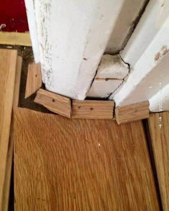 A close-up of terrible carpentry work where small, mismatched wooden molding wedges are crudely nailed down to bridge a gap around a door frame, showing a clear flooring design fail.