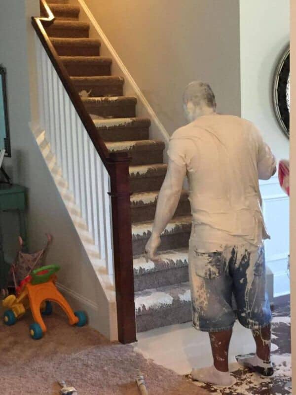 Man covered head-to-toe in white paint looking at a heavily paint-splattered carpeted staircase.