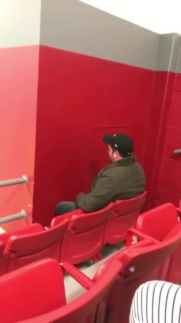 Man in a stadium seat staring directly into a solid red support wall blocking his view.