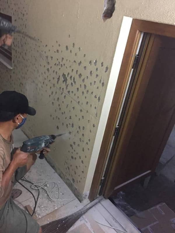 Construction worker using a power drill to make dozens of random holes in a wall.