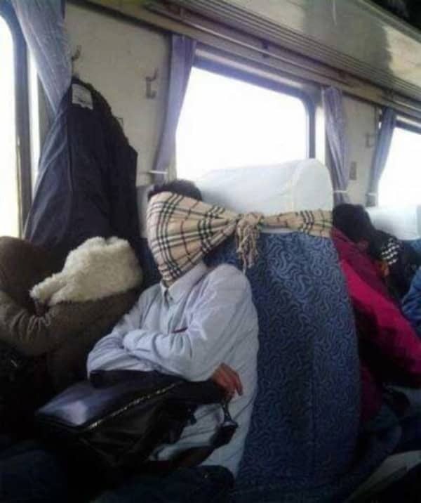 Passenger on a train with a plaid scarf wrapped tightly around their face and the headrest.