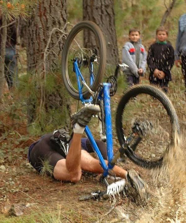 Cyclist crashed upside down in the mud with legs tangled in a blue bicycle frame.