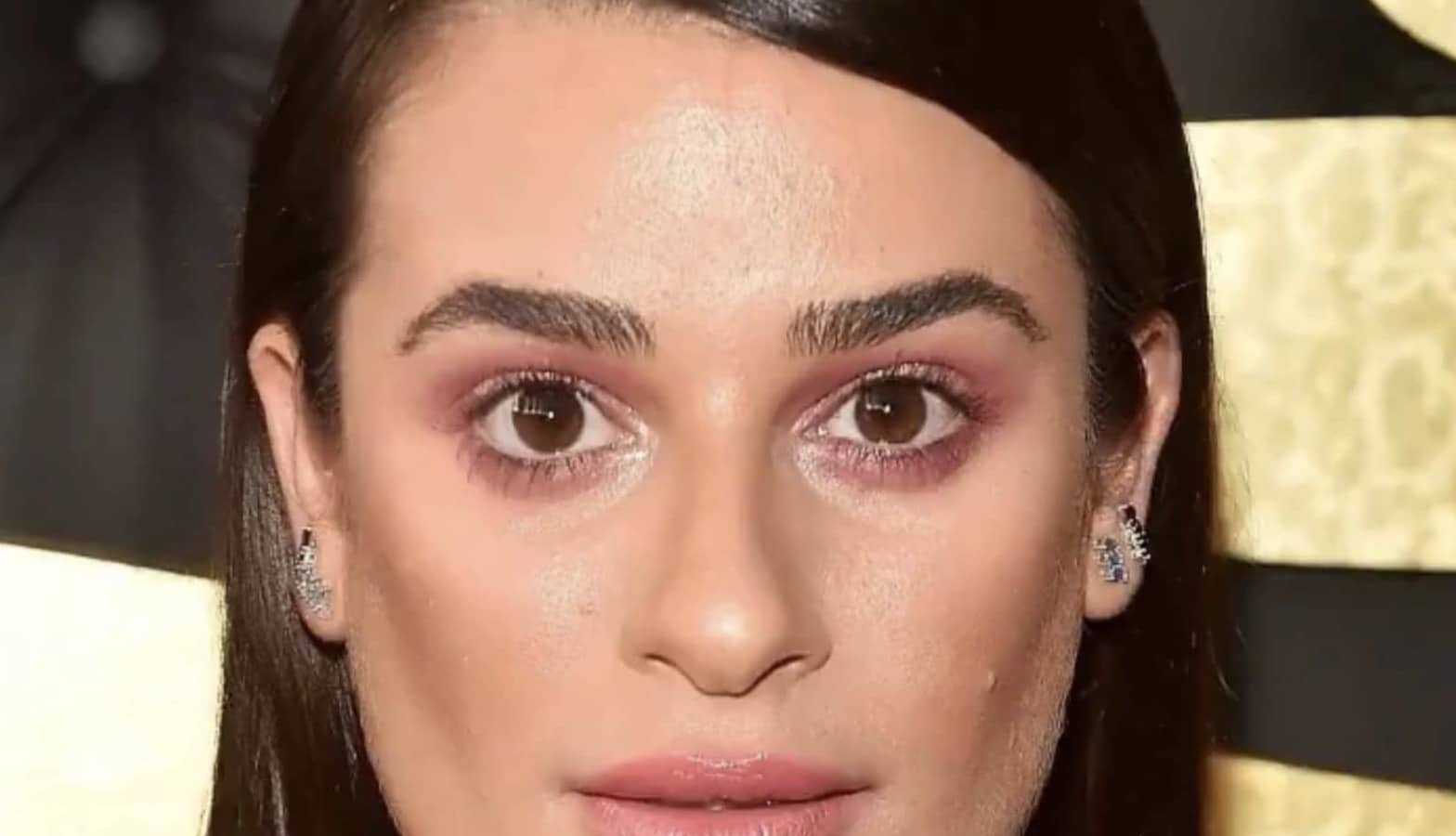 Red carpet portrait of actress Lea Michele staring forward with subtle pink makeup.
