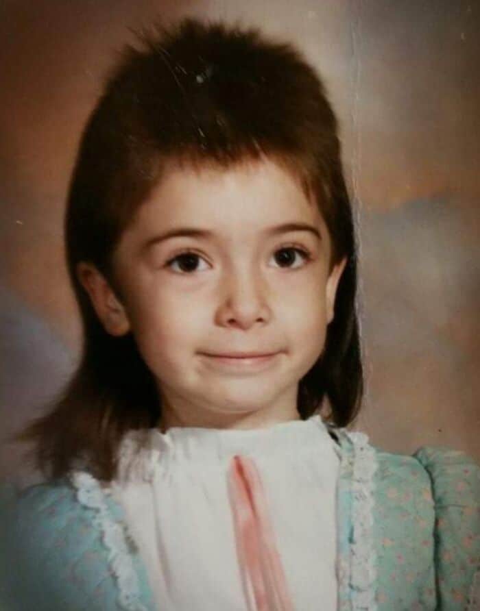 Retro school portrait of a young girl with an aggressively layered spikey mullet haircut.