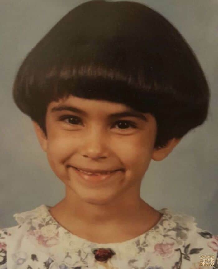 Young smiling girl with a perfectly round, thick dark brown bowl cut hairstyle.