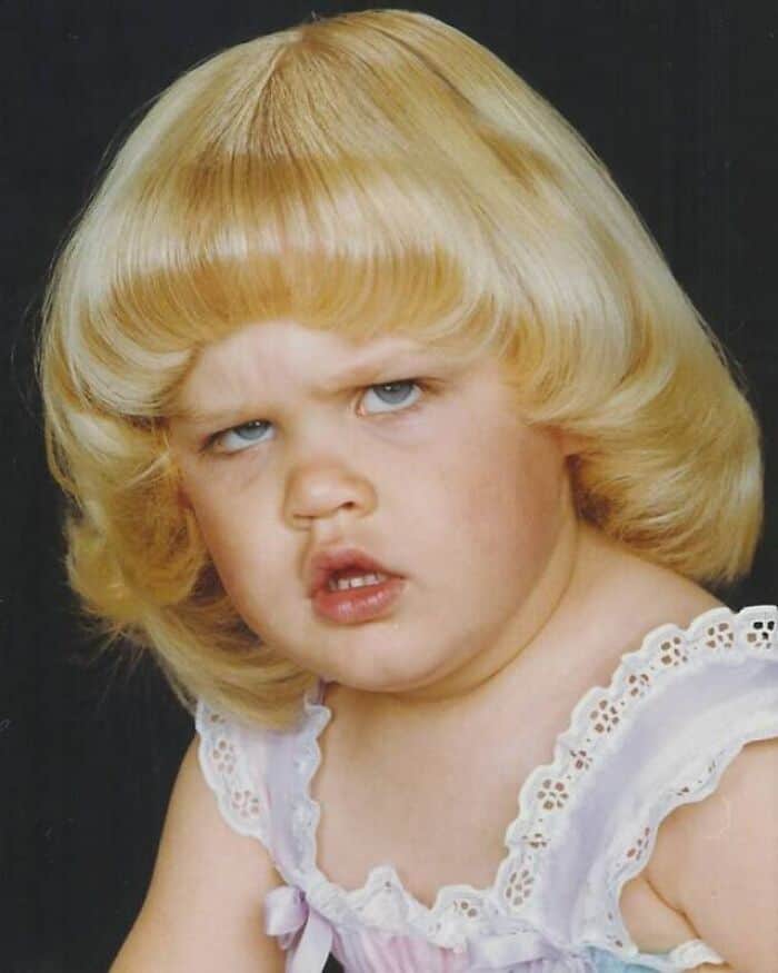 Grumpy little blonde girl with a thick pageboy style bowl haircut staring off-camera.