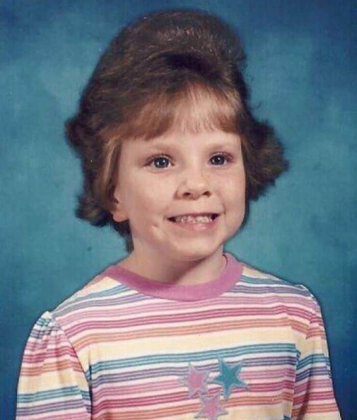 Young girl smiling in a striped shirt with massive, teased hair sprayed up high.