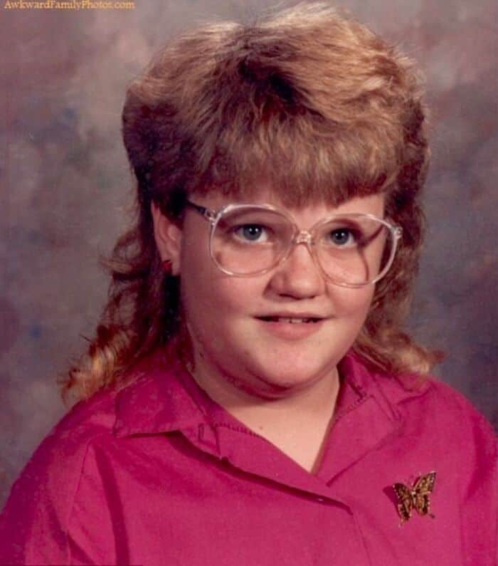 Retro portrait of a girl with giant clear glasses and a heavily feathered mullet.
