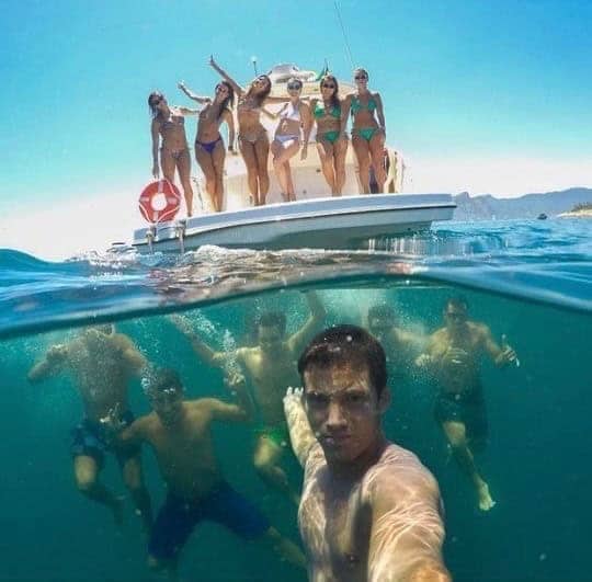 Split-screen view showing women posing on a boat deck and men swimming underwater.